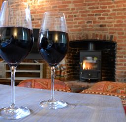 Two glasses of red wine on a wooden table with a fireplace and brick wall in the background at The White House with Studio in Wortwell