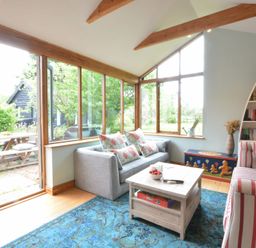 A living room with a gray sofa, striped armchair, blue rug, wooden coffee table, boat shaped bookshelf and windows overlooking a garden at The White House with Studio in Wortwell