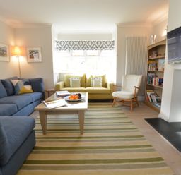 A living room with blue and yellow sofas a striped rug a coffee table a white armchair a bookshelf and a television at Mellows Thorpeness in Thorpeness
