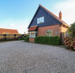 A gravel driveway in front of a house with a tiled roof and a black wooden upper facade at Mellows Thorpeness