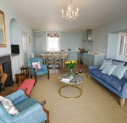 An open plan living room and kitchen with blue sofas wooden dining table and a fireplace at Shingle Skies Aldeburgh