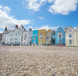 A row of colorful houses along a pebble beach under a partly cloudy sky at Shingle Skies Aldeburgh