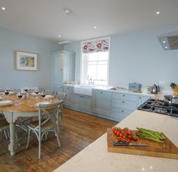 A kitchen with a wooden dining table set for six people and a countertop with vegetables and cooking utensils at Shingle Skies Aldeburgh