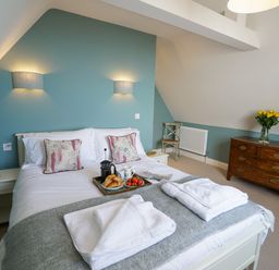 A bedroom with a double bed bedside tables a wooden dresser and a chair at Shingle Skies Aldeburgh