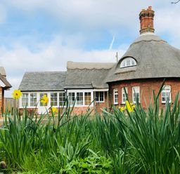 A brick house with a thatched roof and yellow flowers in the foreground at The Round House in Easton near Framlingham
