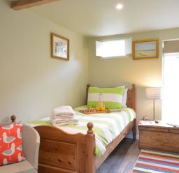 A bedroom with a single wooden bed, a striped chair with a bird cushion, a wooden chest, and framed artworks on the walls at Church Farm Cottage Dunwich Near Westleton