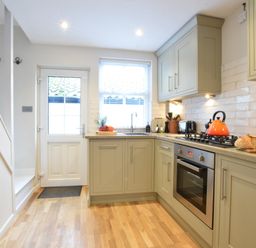 A kitchen with wooden floor cabinets a gas stove oven a sink a white door and a window at 53 Tern Cottage Aldeburgh