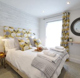 A bedroom with a bed with decorative pillows bedside table and a round mirror on the wall at 53 Tern Cottage Aldeburgh