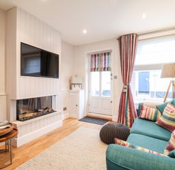 A living room with a teal sofa and striped cushions near a window with matching curtains and a lamp at 51 Tern Cottage Aldeburgh