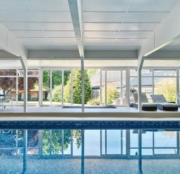 An indoor swimming pool with lounge chairs and a ping pong table behind glass windows at Bedingfield House nr Debenham Debenham