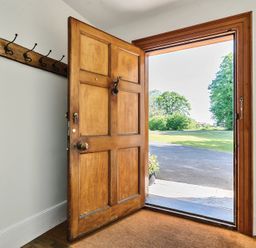 An open wooden front door showing a driveway and lawn outside with coat hooks on the interior wall at Bedingfield House nr Debenham Debenham