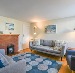 A living room with two grey sofas a blue armchair a blue rug with circular patterns a red brick fireplace and paintings on the wall at Seaflower Aldeburgh in Aldeburgh