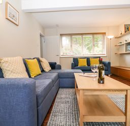 A living room with blue sofas yellow cushions a wooden coffee table and books on shelves at Town Farm House Orford