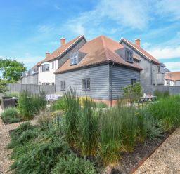 A garden with gravel paths and various plants around a gray wooden house with a tiled roof at Corner Cottage Thorpeness