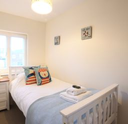 A bedroom with a single bed pillows bedside table with lamp and blue vase at Smugglers Rest Aldeburgh