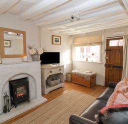 A living room with a white brick fireplace a wooden chest and a leather sofa at Rosemary Cottage Aldeburgh