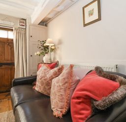 A living room with a black sofa and cushions near a wooden door and a small cabinet at Rosemary Cottage Aldeburgh