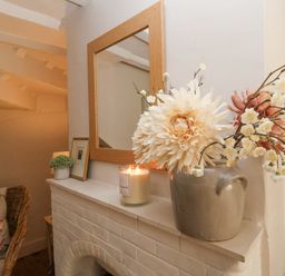 A fireplace mantel with a candle a small plant a framed picture and a vase with flowers and a mirror above at Rosemary Cottage Aldeburgh