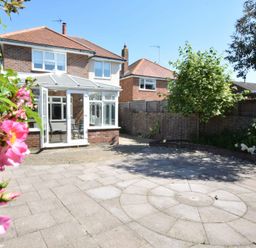 A backyard with paved circular patio area a conservatory on a brick house and plants including a tree and flowers at Napier House Southwold