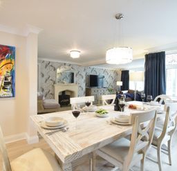 A dining area with a wooden table set with bowls glasses and wine bottles next to a living room with a fireplace and television at Napier House Southwold
