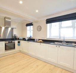 A kitchen with white cabinets black countertops a stainless steel oven and sink at Napier House Southwold