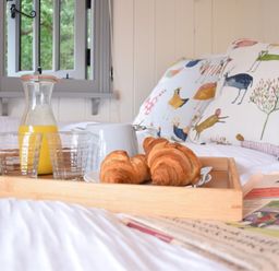 A breakfast tray with croissants orange juice and a white jug on a bed with animal print cushions at Shepherds Pightle in Hollesley