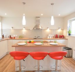 A kitchen with an island and three red stools at Bramertons Nest Long Melford