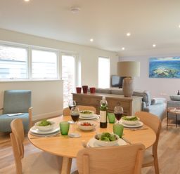 A dining table set with plates bowls of salad glasses of wine and a bottle in a living room with sofas a lamp and a painting at Bramertons Nest Long Melford