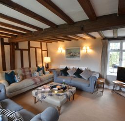 A living room with wooden ceiling beams sofas a TV and a window at Old Valley Farm in Walberswick