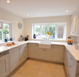 A kitchen with white cabinets a farmhouse sink under a window and various kitchen items on countertops at Old Valley Farm in Walberswick