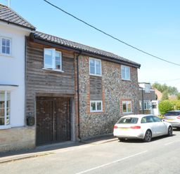 A street view with parked cars and houses with brick and wood exterior at May Barn Ixworth in Bury St Edmunds