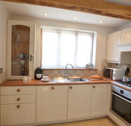 A kitchen with white cabinets wooden countertops a sink oven microwave and a window at May Barn Ixworth in Bury St Edmunds