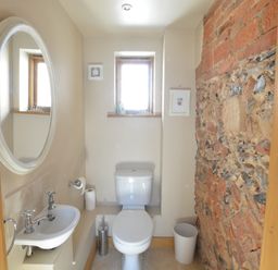 A small bathroom with a toilet a sink a round mirror a window and a brick wall at May Barn Ixworth Bury St Edmunds