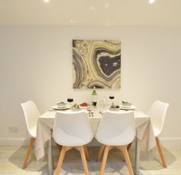 A dining room with a table set for four with white chairs and a patterned painting on the wall at The Smokehouse Cottage in Southwold