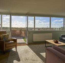 A living room with a sofa and chair near large windows at Harbour Lights in Southwold