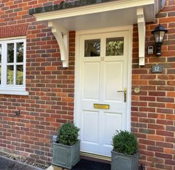 A white front door with two windows and a brass letterbox surrounded by red brick walls with two potted plants on either side
