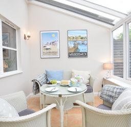 A small sunroom with wicker chairs and a table set with fruit and tea at Bluebelle Cottage Peasenhall