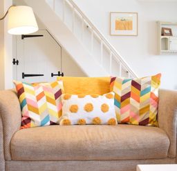 A beige sofa with colorful patterned cushions and a lamp beside it under stairs at Satis Cottage Westleton