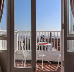 A balcony with a white table and two chairs with books, a bottle, and two glasses seen through glass doors at Albion House Southwold
