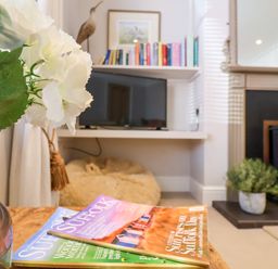 A living room with magazines on a wooden table a TV on a shelf and a fireplace at Albion House Southwold