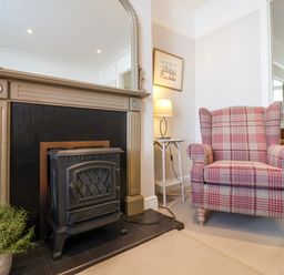 A fireplace with a black stove and a plaid armchair next to a small side table with a lamp at Albion House Southwold