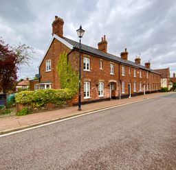 A row of brick houses with chimneys and white windows along a street with a lamppost and parked cars at Rosedene Rickinghall