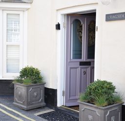 A partially open purple door numbered 9 with two gray planters containing green plants outside and a sign that reads cragside in Aldeburgh