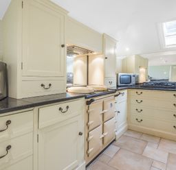 A kitchen with cream cabinets black countertops a stove microwave and a coffee machine at Skelder Parham in Parham Near Framlingham