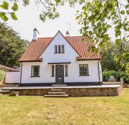 A white house with a red tiled roof a black door and windows surrounded by a garden with grass and trees at High Ground Reydon