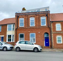 A street view of a brick building with blue doors and several parked cars at Pier View Southwold