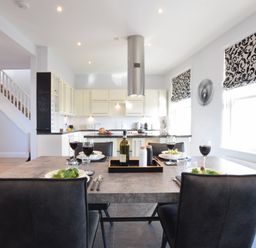 A dining table set with plates glasses and wine in a kitchen with white cabinets and patterned window blinds at Pier View Southwold