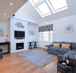 A living room with skylights a gray sofa with yellow cushions and a wall-mounted television at Pier View Southwold