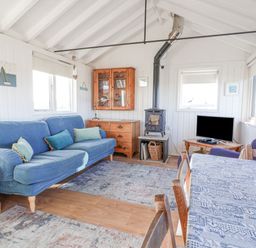 A living room with a blue sofa wood burning stove television and dining table at The Old Fisherman's Hut in Southwold