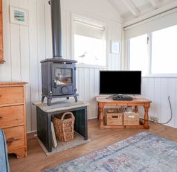 A living room with a wood burning stove a television on a wooden table and wooden drawers at The Old Fisherman's Hut in Southwold